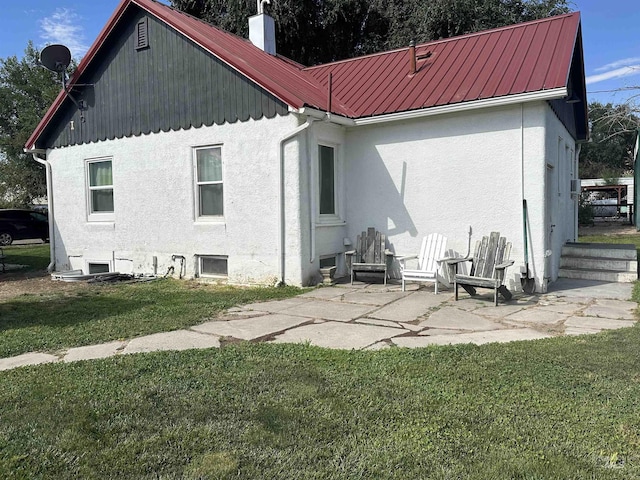 back of property with metal roof, a patio, a yard, stucco siding, and a chimney