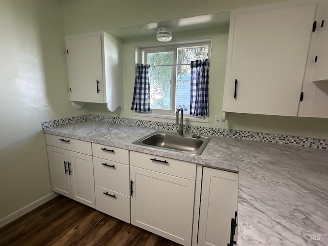 kitchen with dark wood-style floors, light countertops, white cabinets, a sink, and baseboards