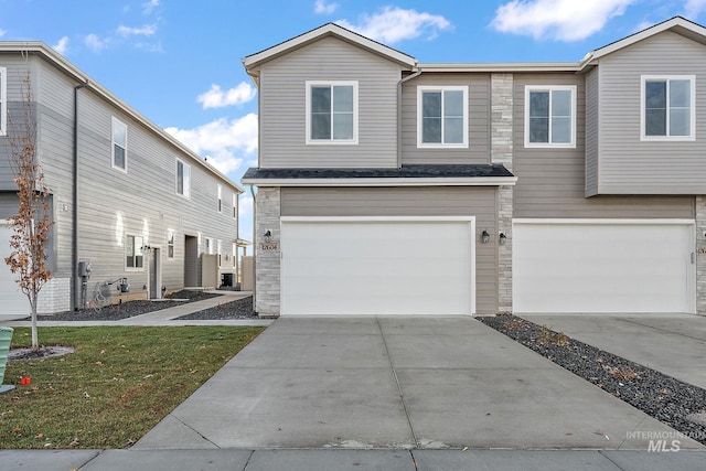 multi unit property featuring a front lawn, stone siding, concrete driveway, an attached garage, and a shingled roof