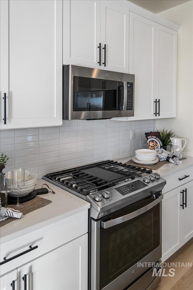 kitchen with stainless steel appliances, backsplash, white cabinets, and light countertops