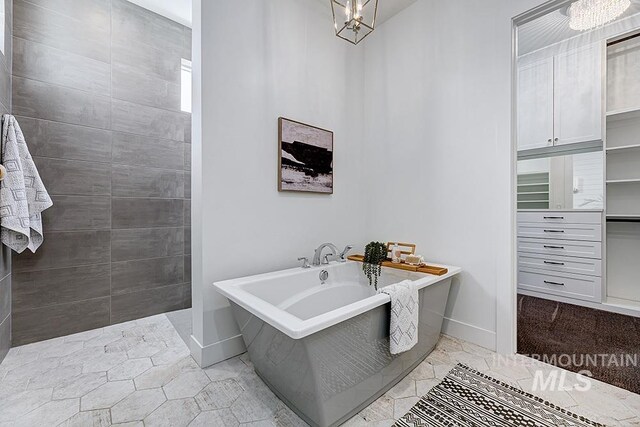 bathroom with an inviting chandelier, tile patterned flooring, and a bathtub