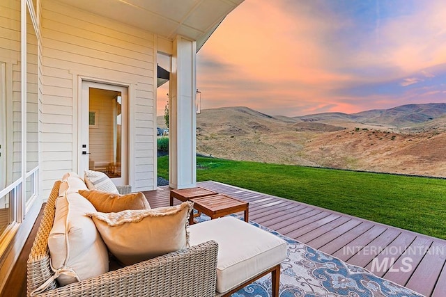 deck at dusk with outdoor lounge area, a yard, and a mountain view