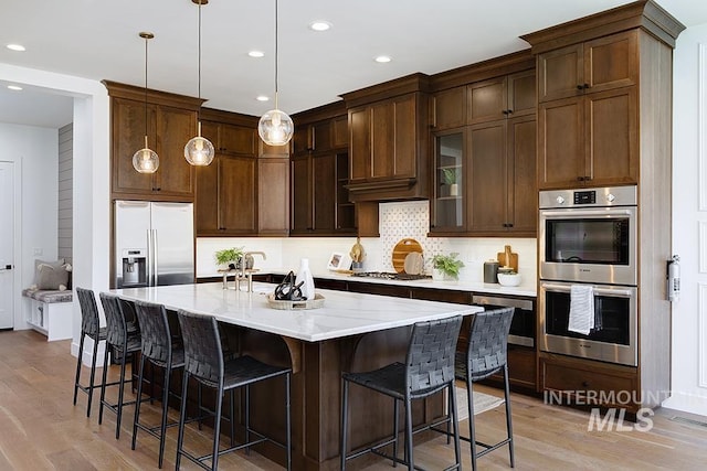 kitchen featuring stainless steel appliances, hanging light fixtures, light wood-type flooring, a breakfast bar area, and backsplash