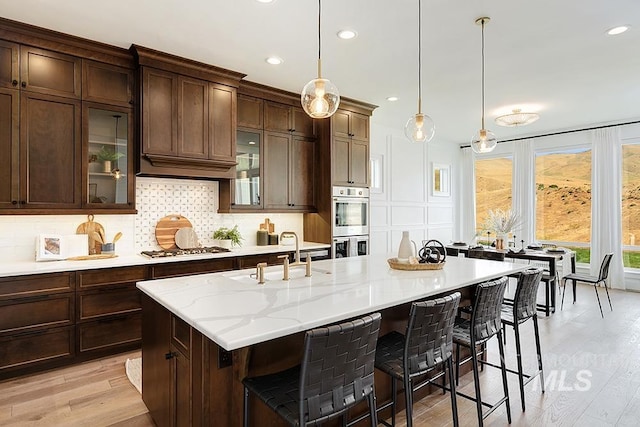 kitchen with hanging light fixtures, light wood-type flooring, sink, a kitchen bar, and backsplash