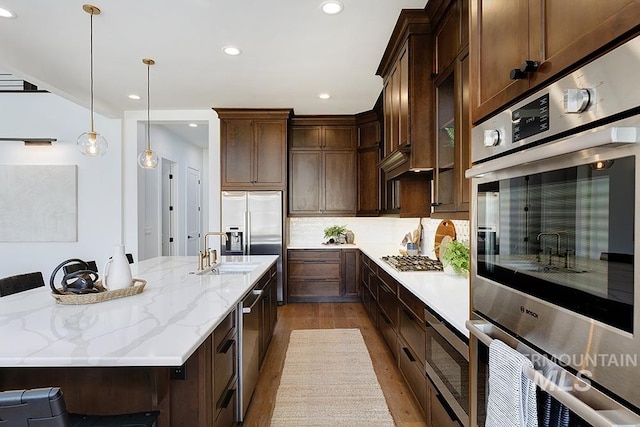 kitchen with stainless steel appliances, sink, light stone countertops, light hardwood / wood-style flooring, and backsplash