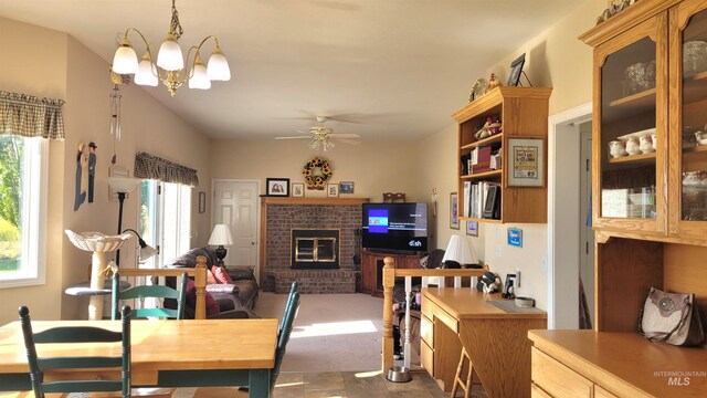 dining space with ceiling fan with notable chandelier and a brick fireplace