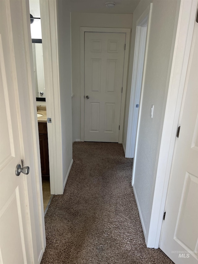 hallway with baseboards and dark carpet