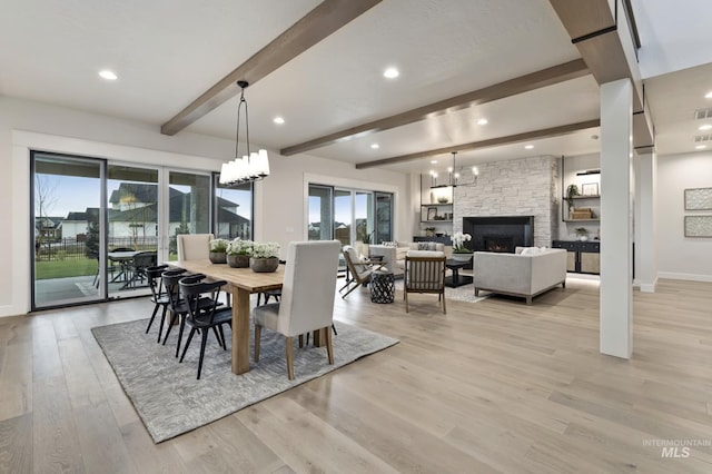 dining area with light hardwood / wood-style floors, a stone fireplace, and beam ceiling