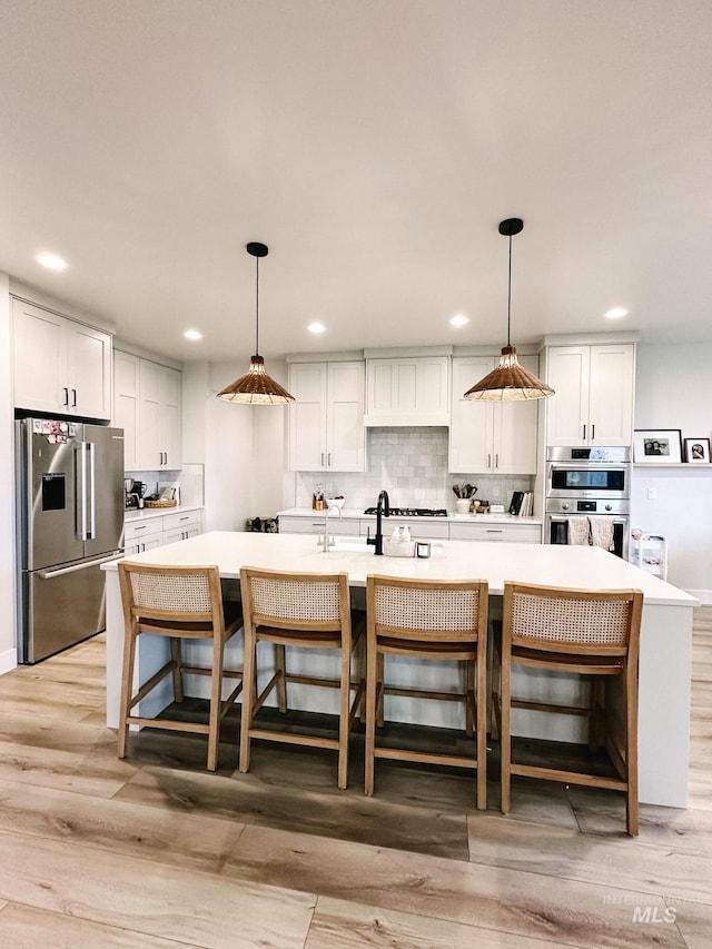 kitchen with pendant lighting, a center island with sink, light hardwood / wood-style flooring, white cabinetry, and stainless steel appliances