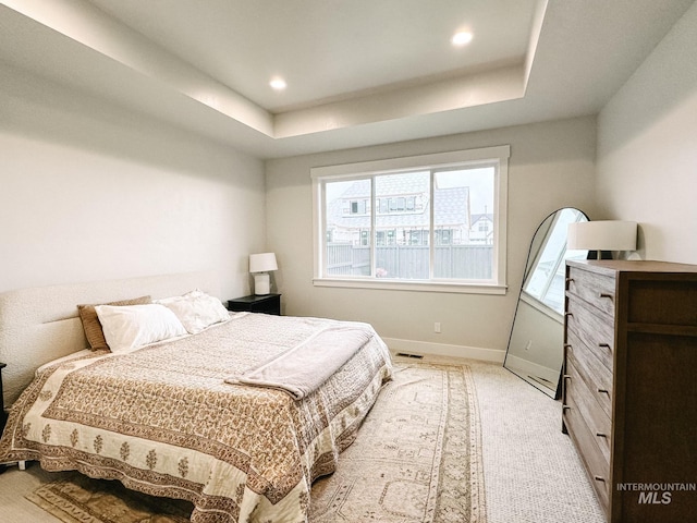 bedroom with light colored carpet and a tray ceiling