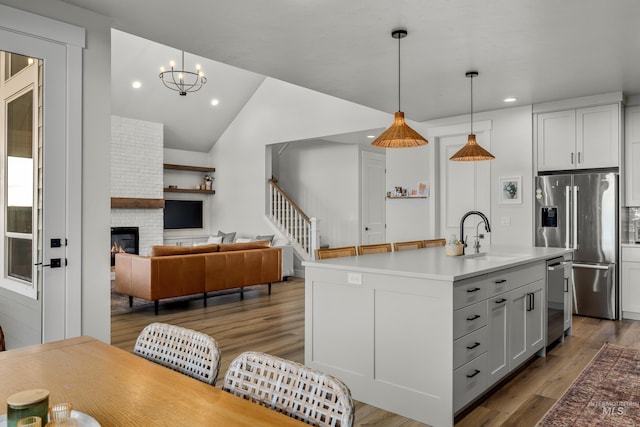 kitchen with hanging light fixtures, stainless steel fridge, sink, and a kitchen island with sink