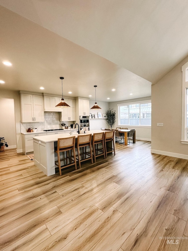 kitchen with white cabinets, pendant lighting, light hardwood / wood-style flooring, and a kitchen island with sink