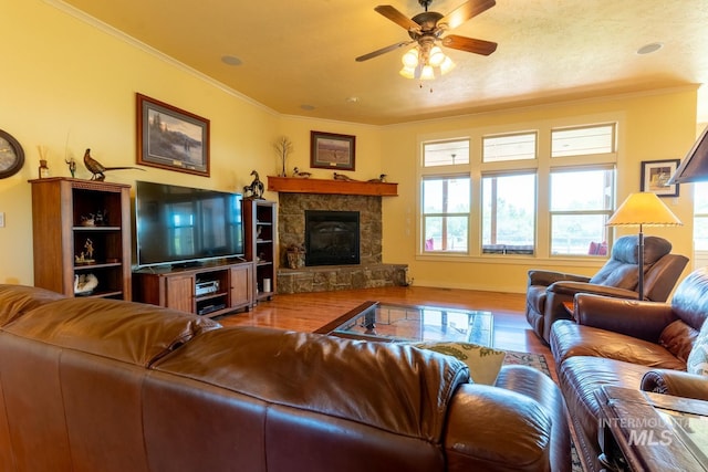 living room with hardwood / wood-style flooring, ceiling fan, ornamental molding, and a stone fireplace