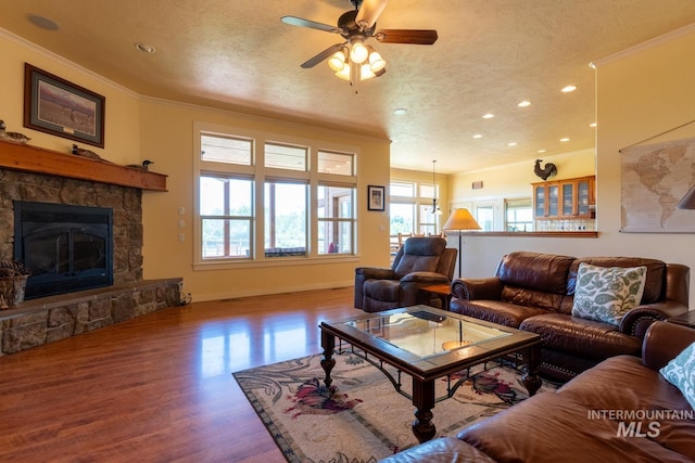 living room with crown molding, a stone fireplace, a textured ceiling, and hardwood / wood-style flooring