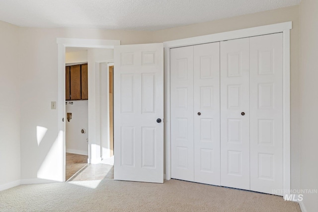 unfurnished bedroom with a textured ceiling, light colored carpet, and a closet