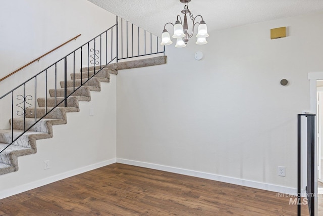 staircase featuring a textured ceiling, an inviting chandelier, and hardwood / wood-style flooring