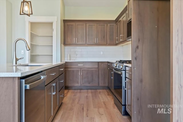 kitchen featuring light wood-style flooring, stainless steel appliances, a sink, hanging light fixtures, and backsplash