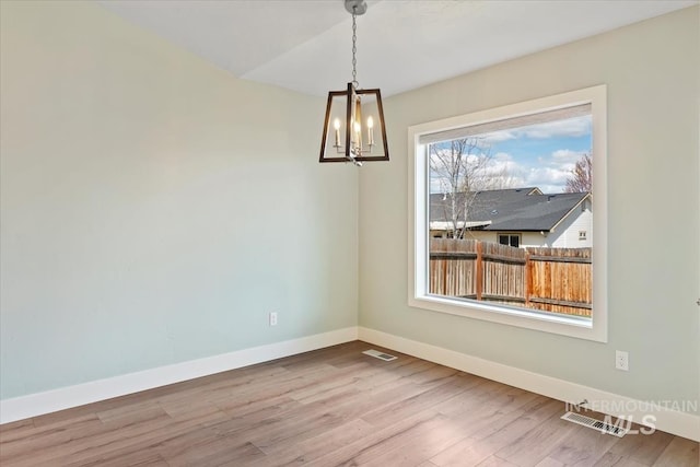 unfurnished dining area with wood finished floors, a notable chandelier, baseboards, and visible vents