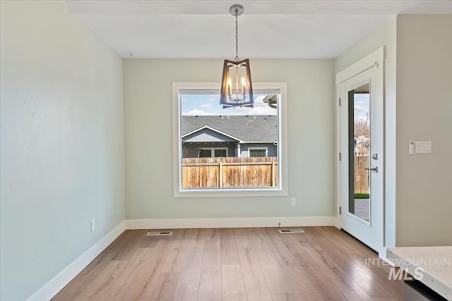 unfurnished dining area with baseboards, visible vents, wood finished floors, and a chandelier