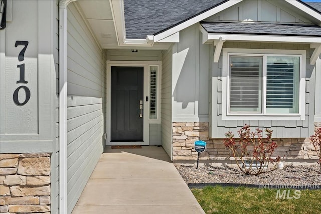 doorway to property featuring stone siding and roof with shingles