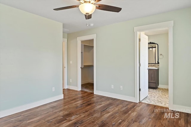 unfurnished bedroom with a walk in closet, baseboards, a ceiling fan, a closet, and wood finished floors