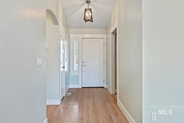 foyer with arched walkways, baseboards, and light wood-style flooring