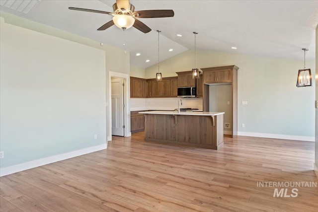 kitchen featuring stainless steel microwave, light countertops, a ceiling fan, and light wood-type flooring