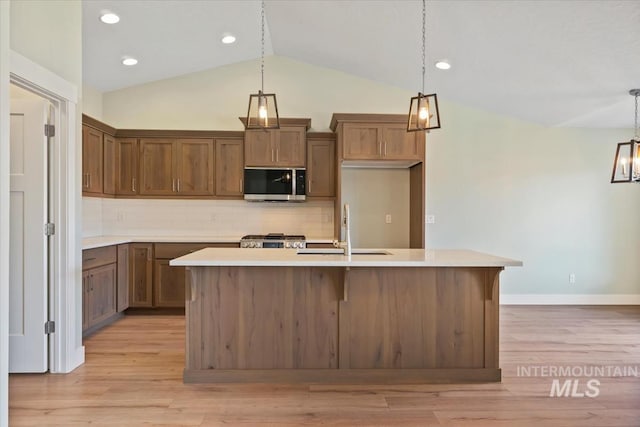 kitchen with a sink, an island with sink, stainless steel microwave, and backsplash