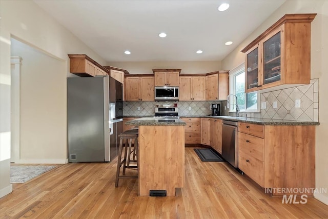 3052 N Christian Way, Meridian, ID 83646 - kitchen with stainless steel appliances, a kitchen island, a breakfast bar area, light wood-style flooring, and glass insert cabinets