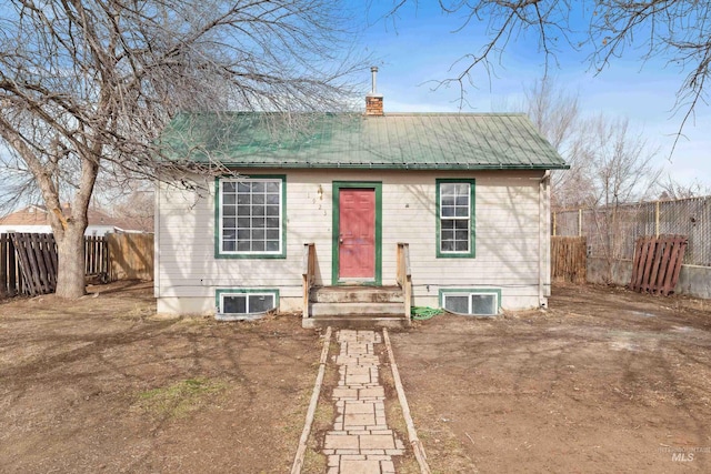 bungalow-style home with entry steps, metal roof, a chimney, and fence