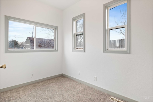 empty room featuring carpet floors, visible vents, and baseboards