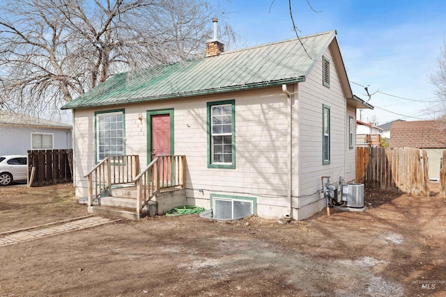 bungalow featuring central air condition unit, a chimney, fence, and metal roof