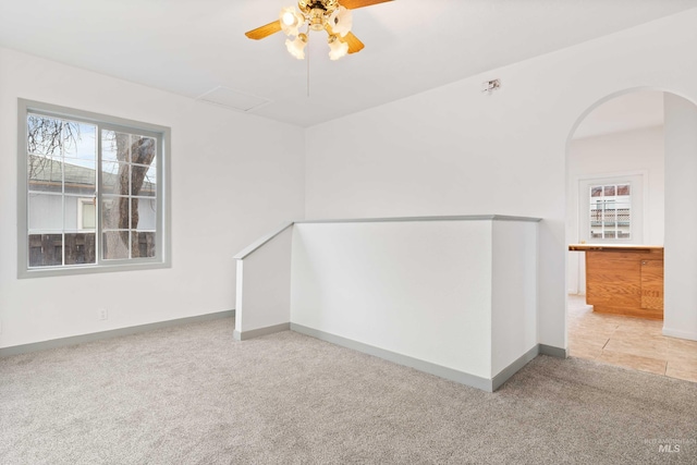 empty room featuring attic access, baseboards, arched walkways, ceiling fan, and carpet floors