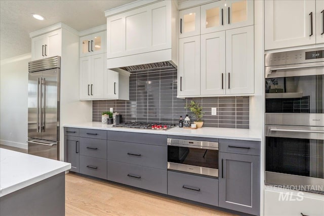 kitchen with gray cabinets, light wood-type flooring, white cabinetry, and appliances with stainless steel finishes