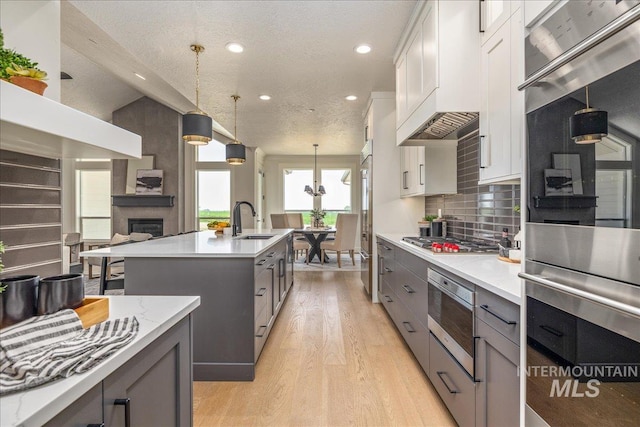 kitchen with appliances with stainless steel finishes, gray cabinets, white cabinetry, and an island with sink