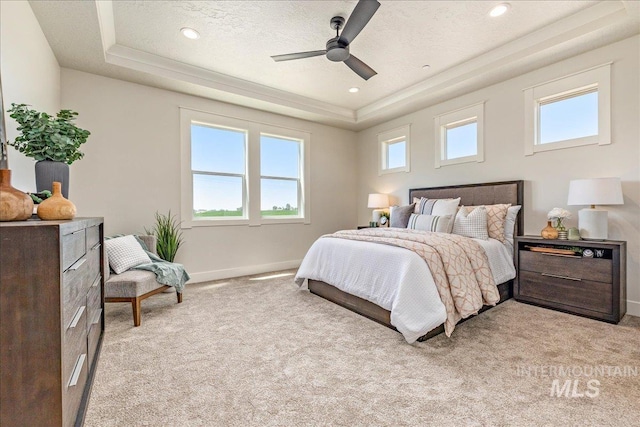 carpeted bedroom featuring multiple windows, a textured ceiling, a tray ceiling, and ceiling fan