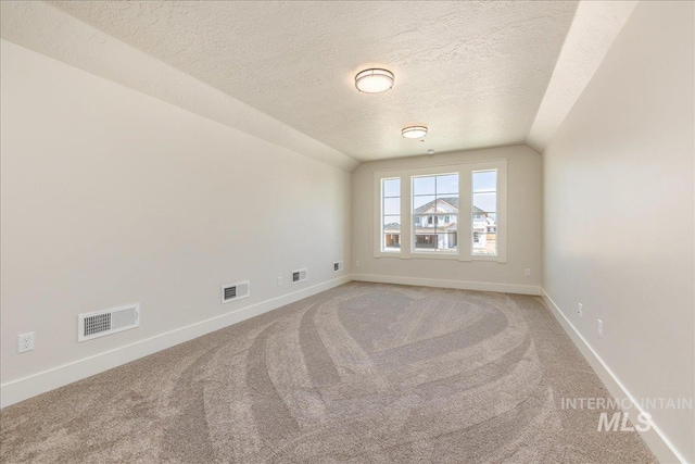 empty room featuring a textured ceiling, carpet floors, and vaulted ceiling