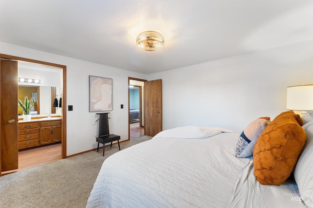 bedroom featuring light colored carpet, baseboards, ensuite bathroom, and a sink