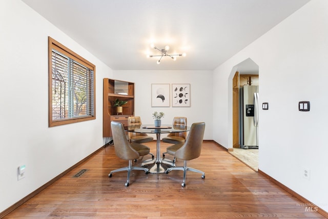 dining space with arched walkways, light wood-type flooring, and baseboards