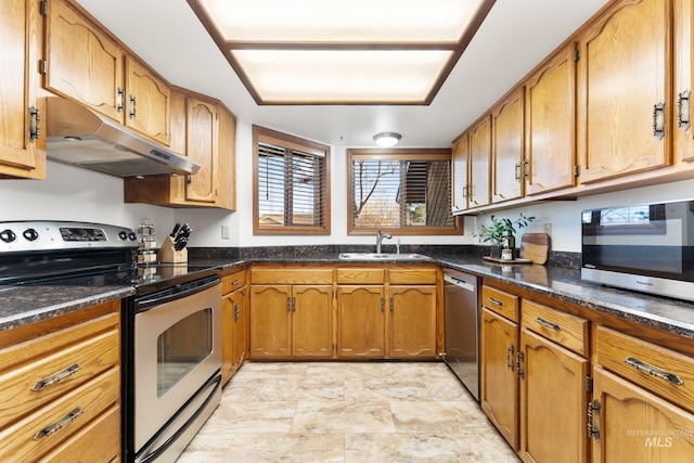 kitchen with under cabinet range hood, dark stone countertops, brown cabinetry, stainless steel appliances, and a sink