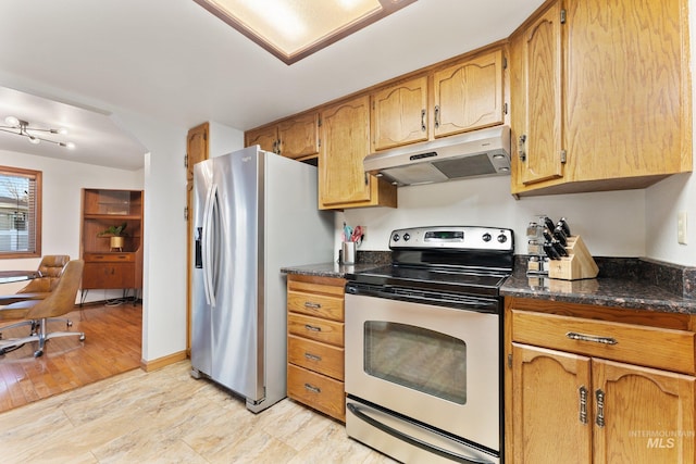 kitchen featuring under cabinet range hood, dark stone countertops, stainless steel appliances, arched walkways, and baseboards