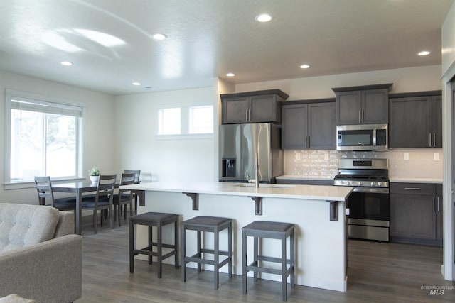 kitchen with a center island with sink, a breakfast bar area, stainless steel appliances, tasteful backsplash, and light countertops