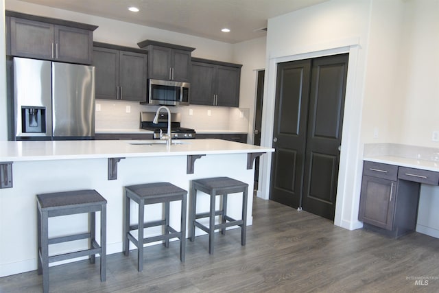 kitchen with stainless steel appliances, a breakfast bar, an island with sink, and light countertops