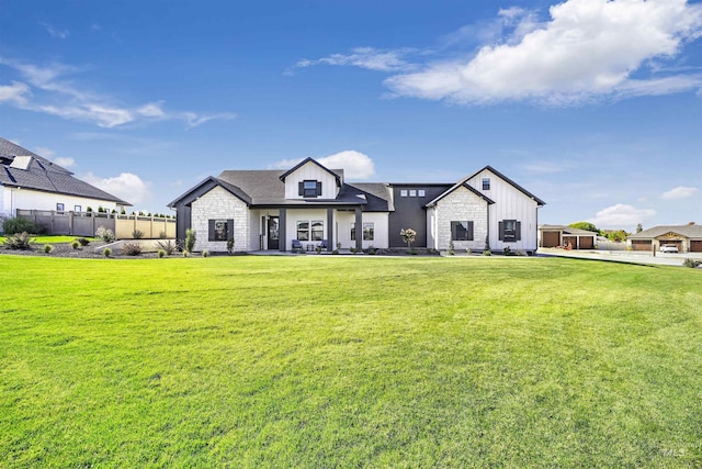 modern farmhouse featuring stone siding, fence, a front lawn, and board and batten siding