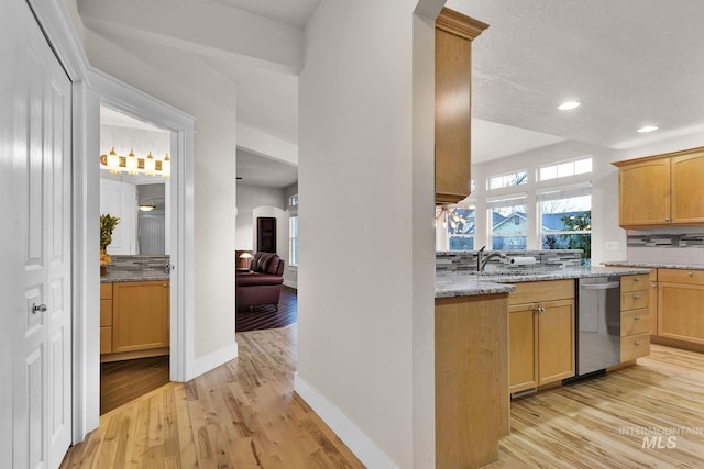 kitchen with arched walkways, stainless steel dishwasher, light wood-type flooring, and decorative backsplash