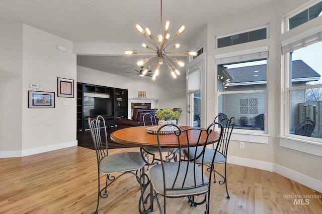 dining room featuring light wood-style floors, baseboards, a fireplace, and a chandelier