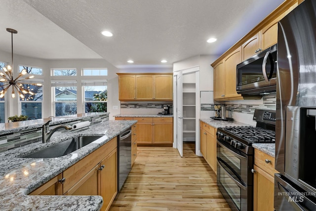 kitchen featuring hanging light fixtures, appliances with stainless steel finishes, a sink, light stone countertops, and light wood-type flooring