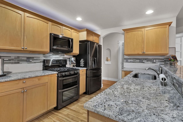 kitchen featuring range with two ovens, a sink, light stone counters, and black fridge