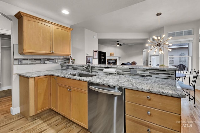 kitchen with a warm lit fireplace, a sink, a peninsula, and dishwasher