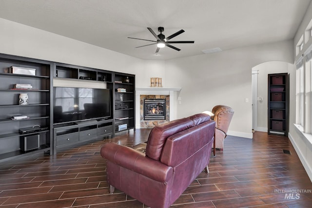 living area with arched walkways, ceiling fan, baseboards, wood tiled floor, and a glass covered fireplace